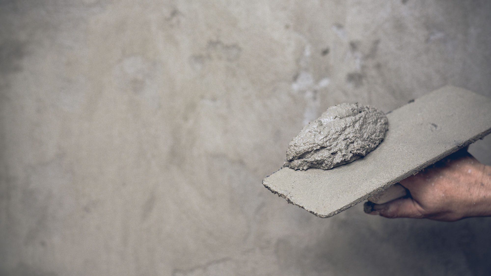 Detalle de una mano sujetando una espátula con cemento